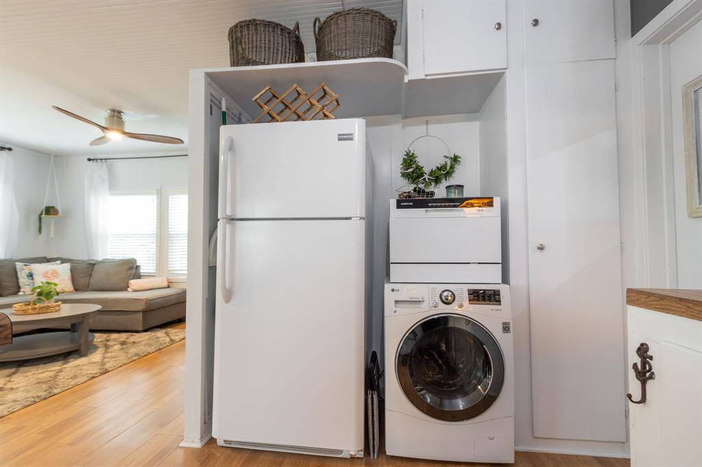 This photo showcases a compact and efficient laundry area with all in one--washer and dryer beside a refrigerator. A compact dishwasher included. The space is integrated into a cozy living area with natural light, and modern decor.