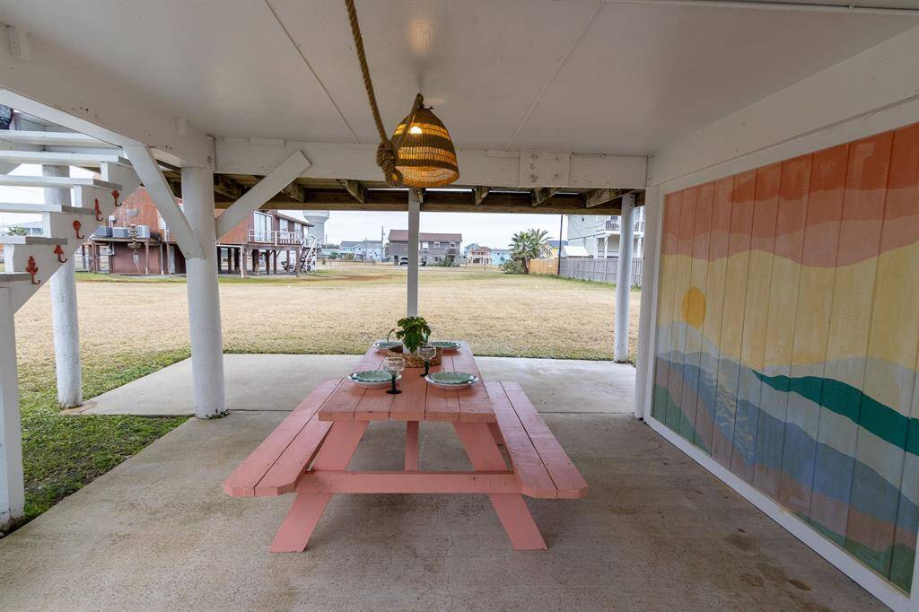 This photo shows a covered patio area with a concrete floor and wooden beams overhead, leading to a spacious grassy yard. The setting is open and quiet, ideal for outdoor activities or relaxing.