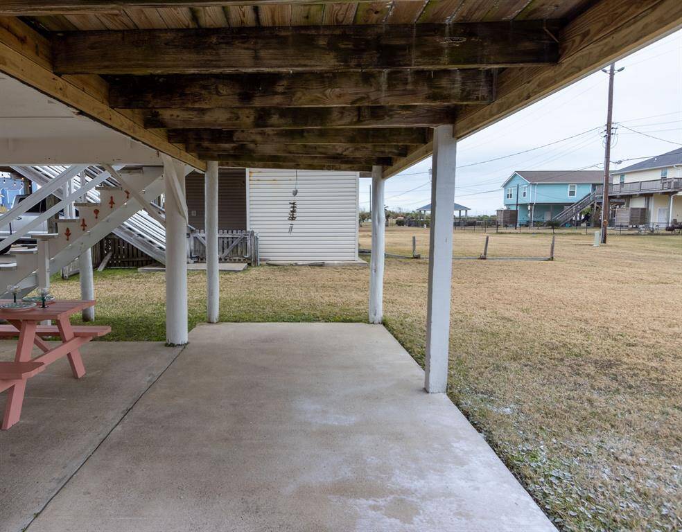 This photo shows a covered patio area with a concrete floor and wooden beams overhead, leading to a spacious grassy yard. The setting is open and quiet, ideal for outdoor activities or relaxing.