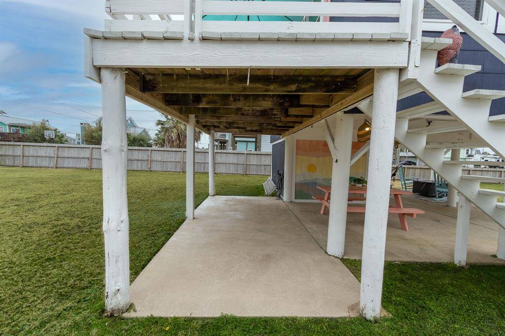 This photo shows a covered patio area with a concrete floor and wooden beams overhead, leading to a spacious grassy yard. The setting is open and quiet, ideal for outdoor activities or relaxing.