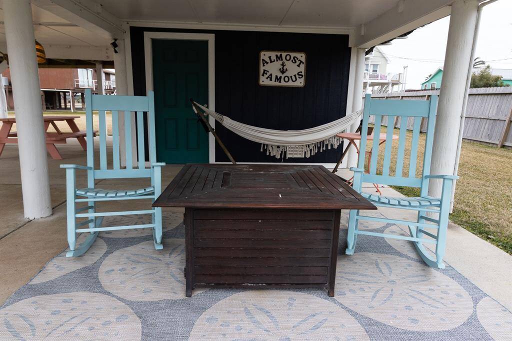 This cozy outdoor space features a covered patio with two turquoise rocking chairs and a hammock. It's perfect for relaxing and enjoying the garden view.