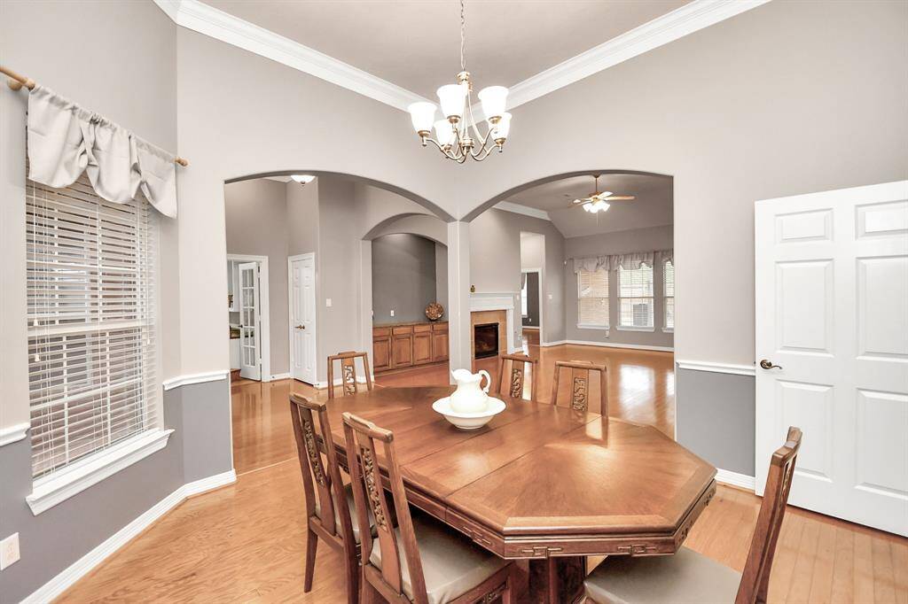 Experience the inviting dining area with elegant crown molding, warm hardwood floors, and a stylish chandelier. Large windows with draped curtains flood the space with natural light, seamlessly connecting to a cozy living room with a fireplace.  12 foot ceilings.