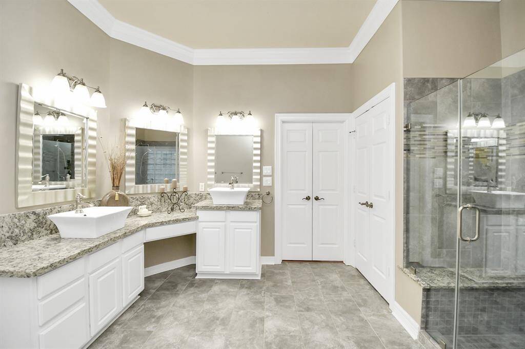 This elegant primary bathroom, remodeled in 2021, features dual sinks, granite countertops, chic lighting, and a large glass shower. The neutral tones and ample storage offer a modern, inviting feel.