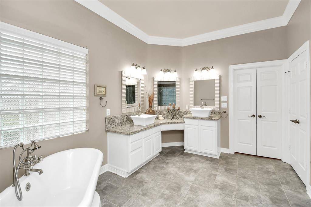 This spacious primary bathroom features a luxurious freestanding tub, dual sinks with granite countertops, and ample storage with elegant cabinetry. The neutral tones and large window provide a bright, inviting atmosphere.
