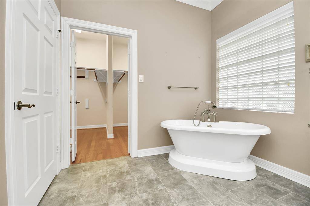 Experience luxury in this 2021 remodeled primary bathroom featuring a freestanding tub, elegant tiled flooring, and a bright window. Enjoy direct access to a spacious walk-in closet with wooden floors and ample shelving.