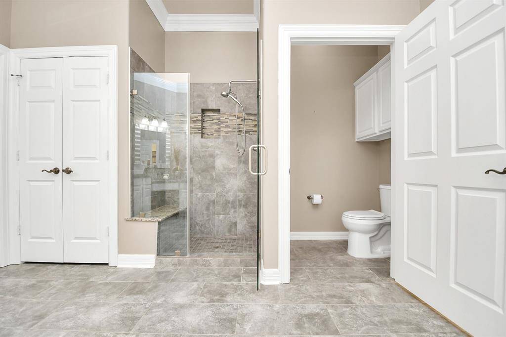 Modernized in 2021, the primary bathroom features a spacious glass shower, elegant tile flooring, and a separate toilet area with sleek white cabinetry.