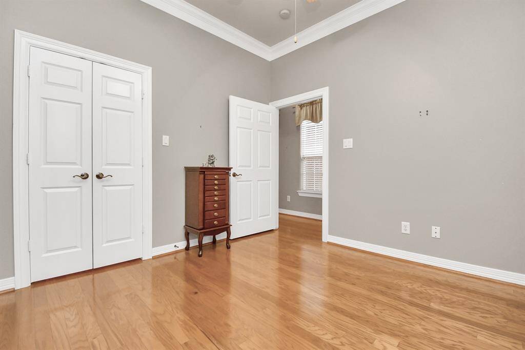 This inviting room showcases hardwood floors, elegant gray walls, and crisp white trim. Enjoy ample storage with a spacious closet. A window bathes the space in natural light, complemented by a ceiling fan for added comfort.