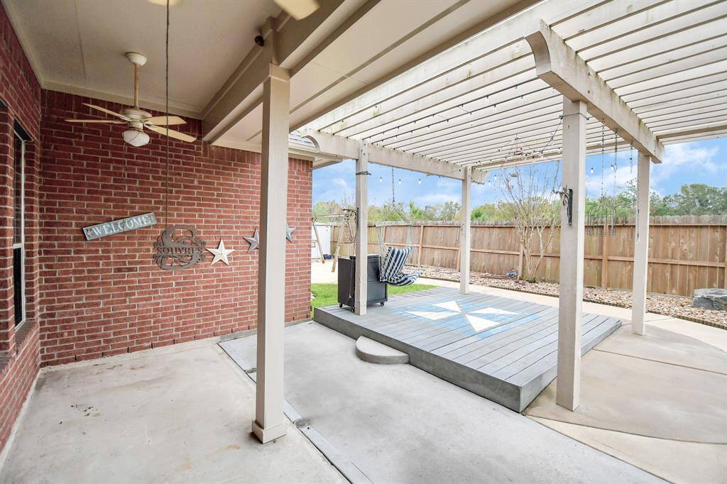 This inviting backyard patio features a charming pergola with string lights, a cozy raised deck for seating, and a wooden fence for privacy—perfect for outdoor relaxation and entertainment.