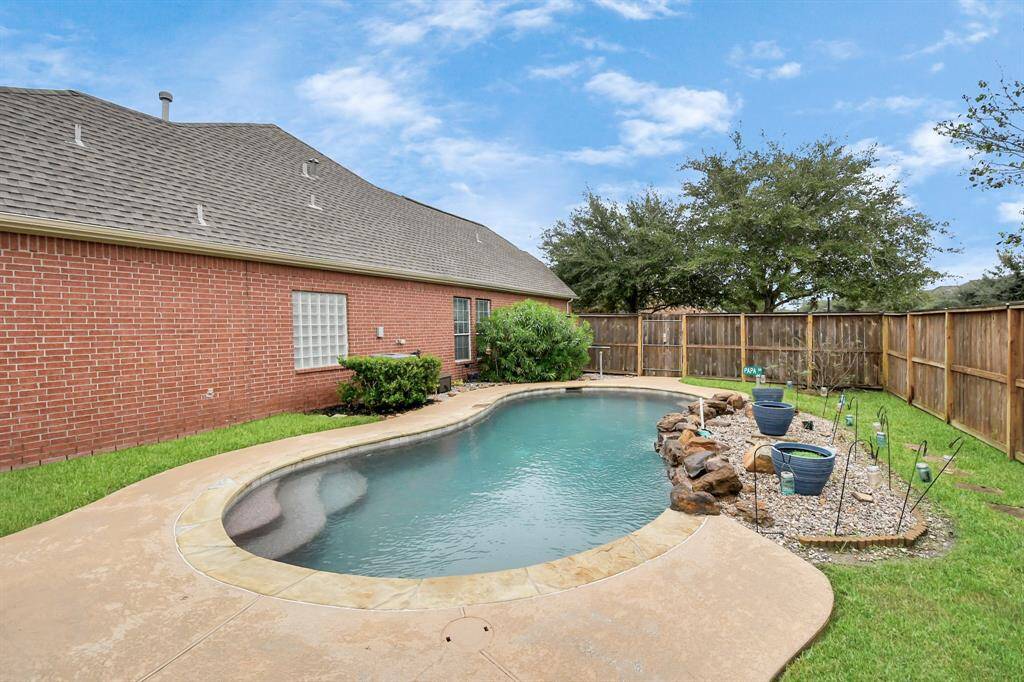 This backyard features a charming in-ground pool with a rock waterfall, surrounded by a well-maintained lawn and privacy fence, perfect for relaxation and entertaining.