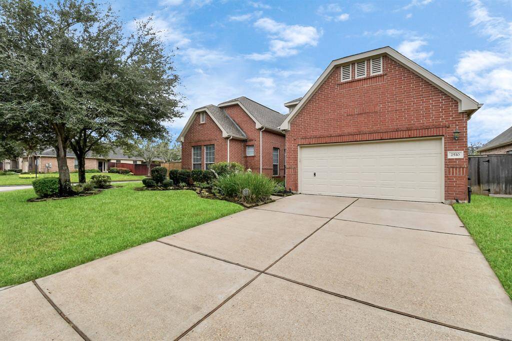Charming brick home with great curb appeal, featuring a well-maintained front yard, lush landscaping, and a spacious driveway leading to a two-car garage with epoxy floors.