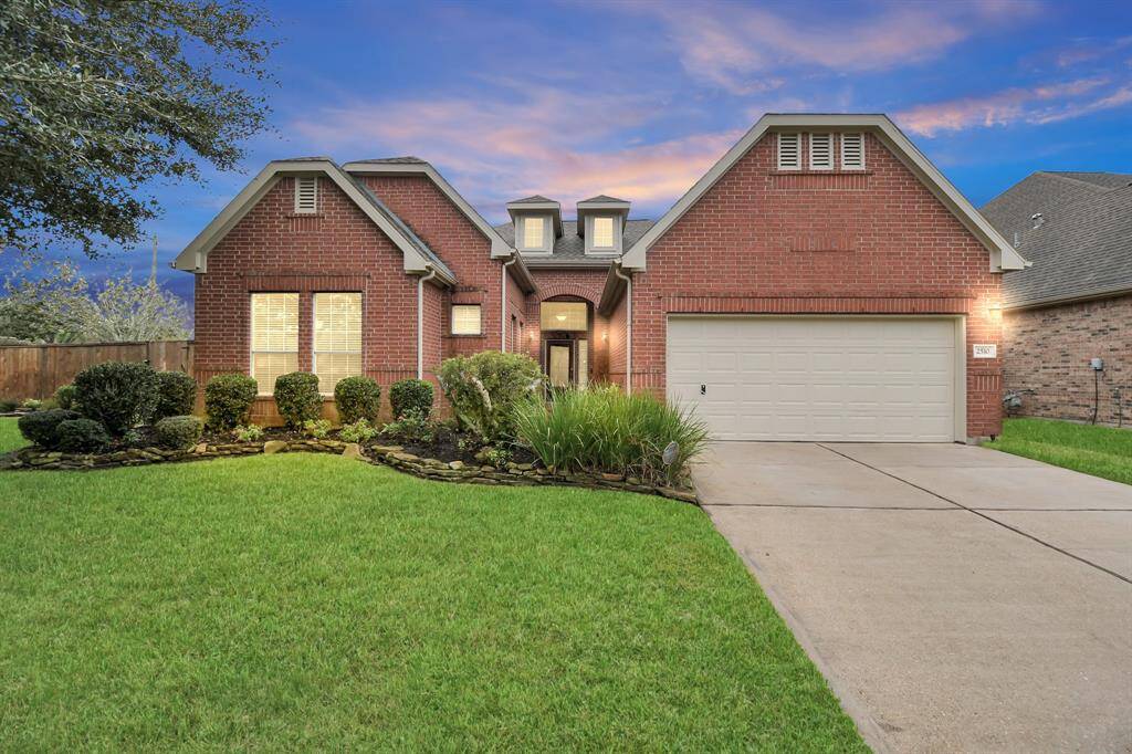 Charming brick home with great curb appeal, featuring a well-maintained lawn and neatly landscaped bushes. It has a two-car garage and a welcoming front entrance under a picturesque sky.