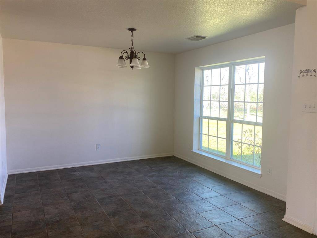 This room features a large window providing ample natural light, a simple chandelier, and dark tiled flooring, creating a bright and inviting space.