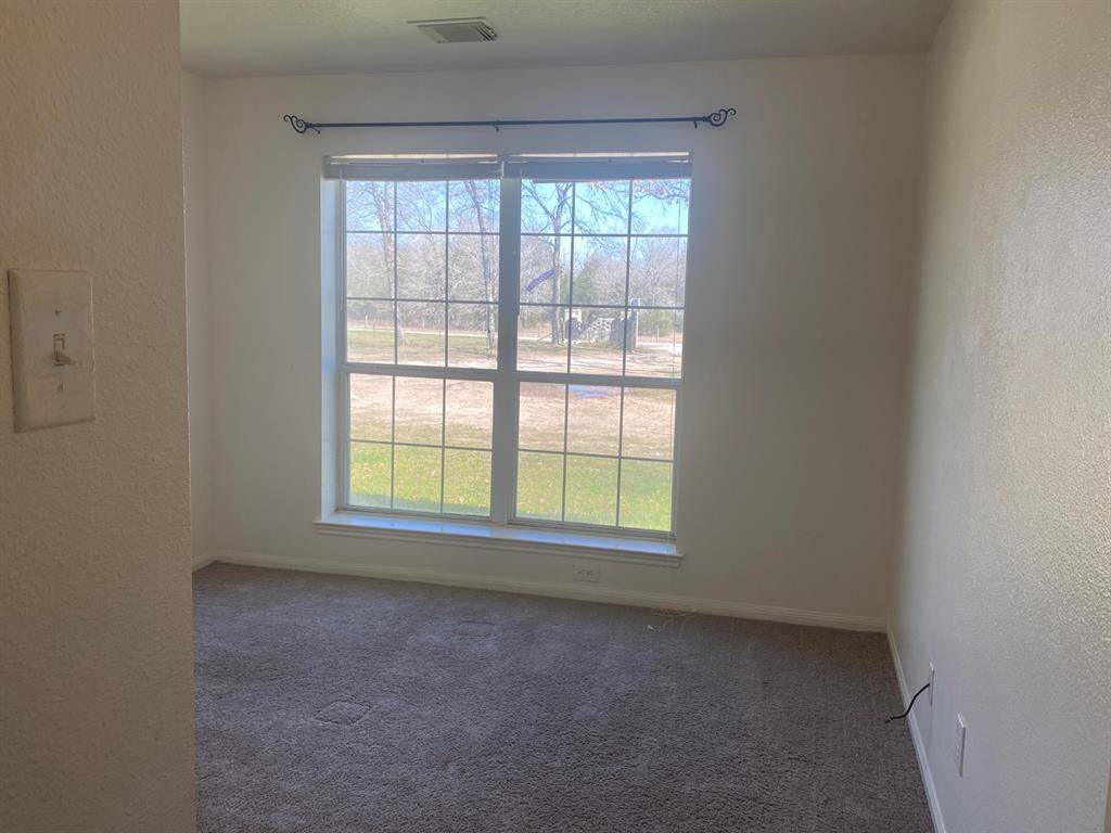 This room features a large window allowing ample natural light, with neutral walls and a carpeted floor, creating a cozy and inviting space.
