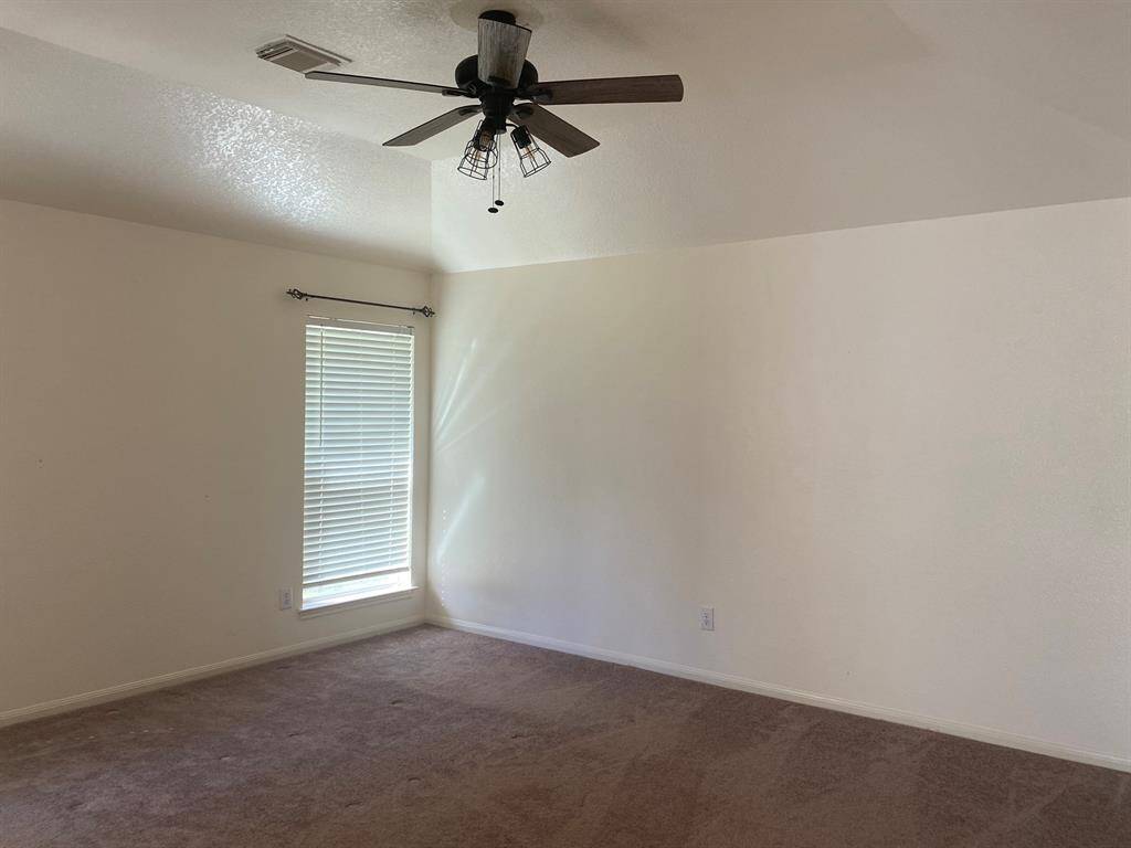 This room features neutral walls, a carpeted floor, a ceiling fan with lights, and a window with blinds, allowing natural light to filter in.