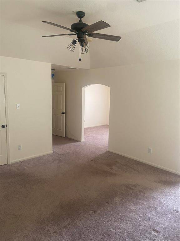 This room features neutral walls and carpet, a ceiling fan, and an arched doorway leading to an adjacent space, creating an inviting and versatile area.