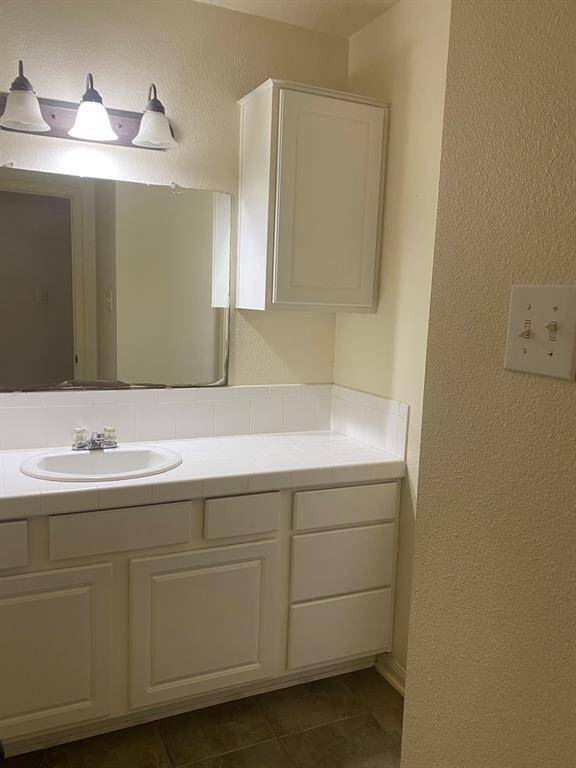 This bathroom features a clean, white vanity with ample cabinet storage, a large mirror, and modern light fixtures, offering a bright and functional space.