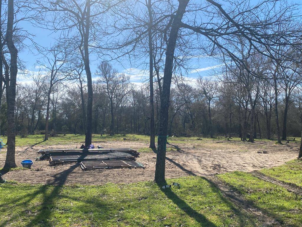 This photo shows a spacious, partially cleared lot with several mature trees, offering a natural setting and potential for development. The presence of construction materials suggests readiness for building, with ample open space and surrounding greenery.