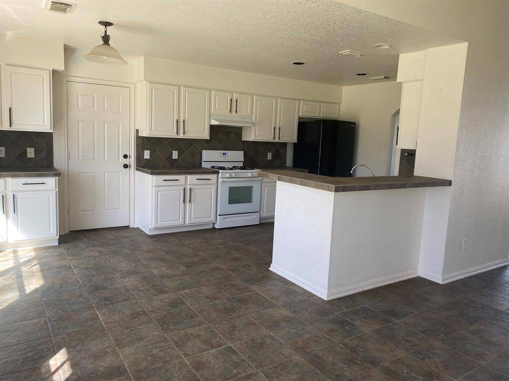 Spacious kitchen with white cabinetry, a gas stove, and a dark tile backsplash. It features a breakfast bar and a tiled floor, offering a clean and modern look.