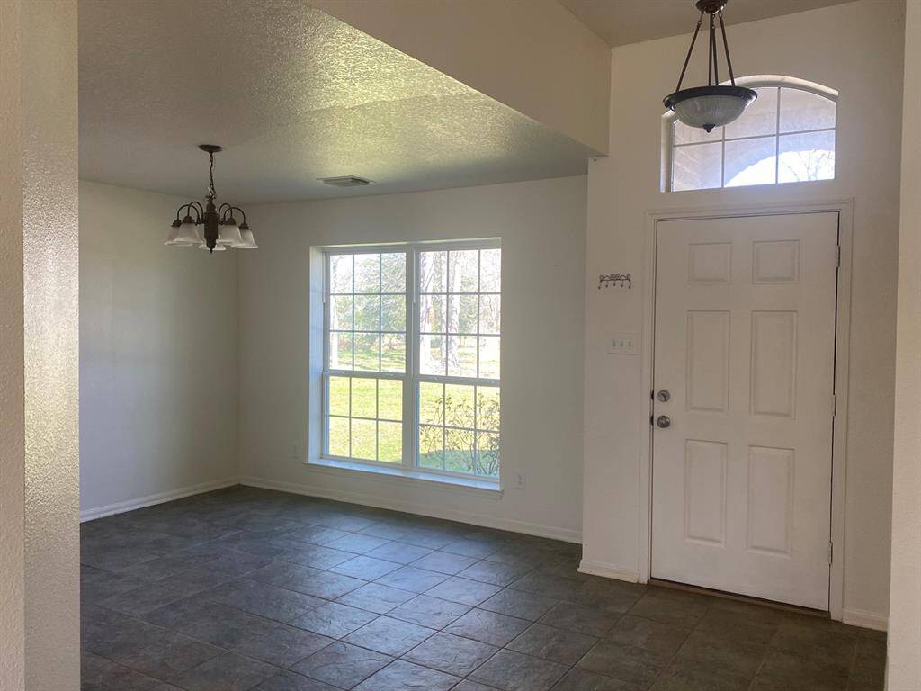 This photo shows a bright entryway with a large window and a white front door. The space features tiled flooring and is illuminated by two ceiling light fixtures, creating a welcoming atmosphere.