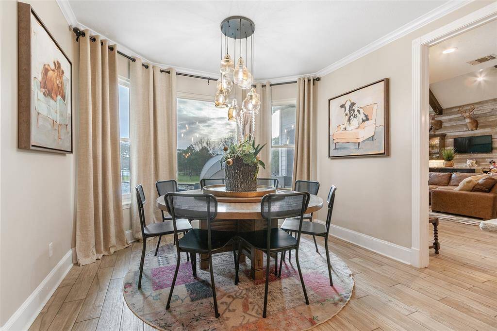 The breakfast area is surrounded by large windows that overlook the backyard.  Large windows provide natural light, while a modern chandelier adds elegance. The space opens into a cozy living area.