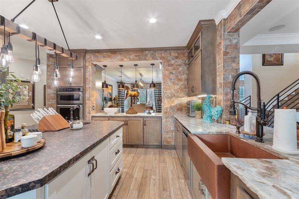 This kitchen includes a large island with a leathered granite countertop, dual ovens, and a stylish farmhouse sink. The open layout provides a view into a cozy dining space, creating a welcoming and functional atmosphere.