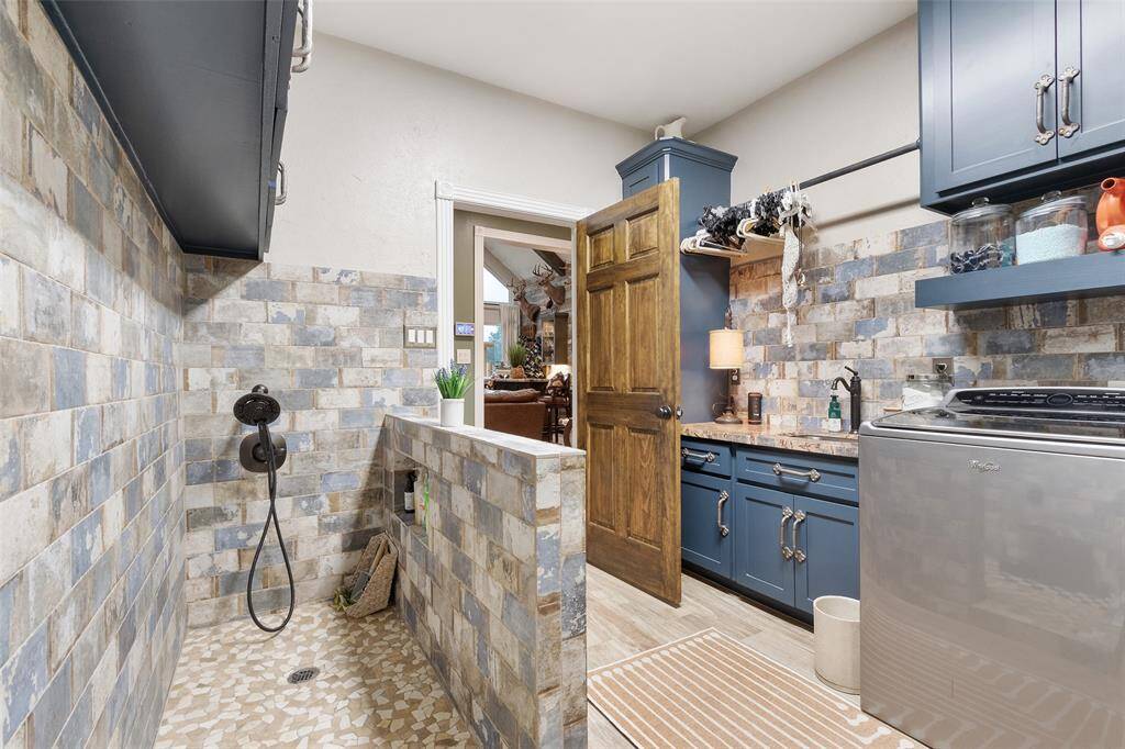 This photo showcases a stylish laundry room with a built-in pet shower, and tile backsplash. The space is functional and welcoming, featuring ample storage.