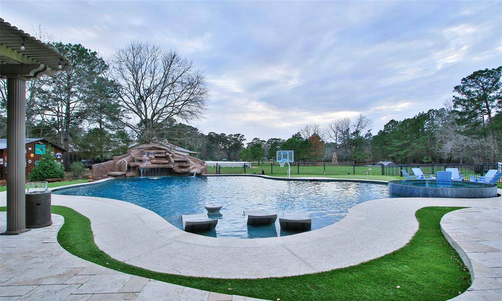 This photo showcases a spacious backyard with a large, pool featuring a tanning ledge, rock waterfall and slide. The pool area offers a serene and private outdoor retreat.
