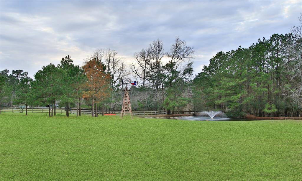 This photo showcases a spacious, grassy yard with a small pond featuring a fountain, surrounded by trees. Fencing adds a rustic charm, offering a serene and picturesque outdoor space ideal for relaxation and recreation.