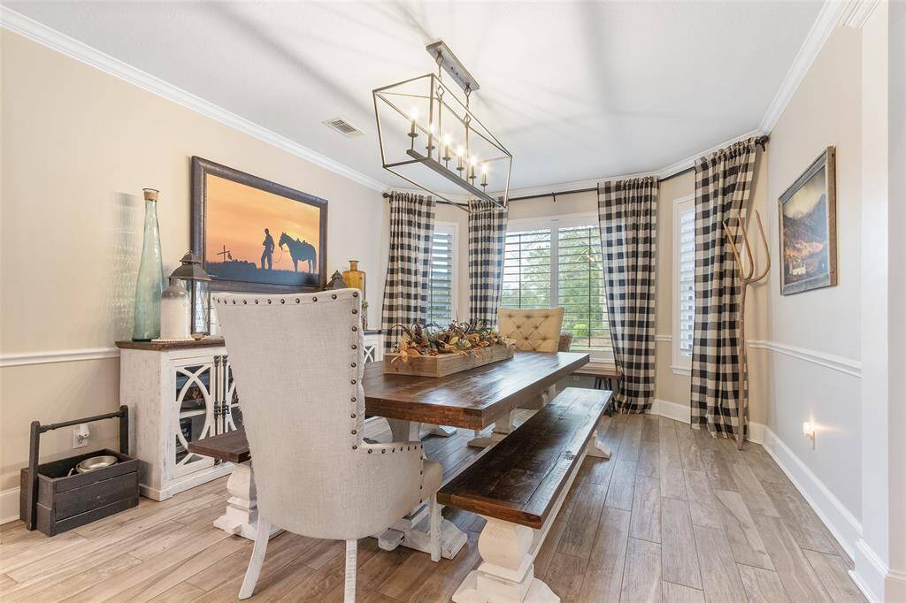 This spacious dining room offers a stunning modern light fixture, wood floors, chair rail, and plenty of windows with shutters to let the natural light in.