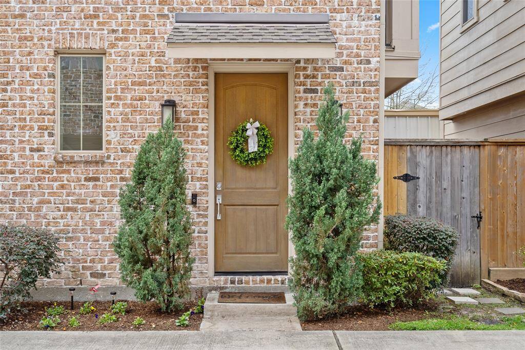 Traditional brick and hardy-plank exterior framed by a pair of mature fir shrubs. An appealing and illuminated entrance is offered, as well as a covered porch awning. Freshly* upgraded landscaping - Feb. 2025 per Seller. The gardener gate is to the immediate right.