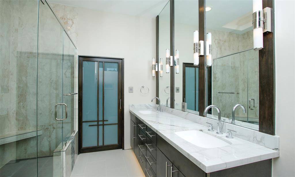 Elegance abounds in this primary bathroom.  Natural Quartzite counter tops with dual sinks and a wall of mirrors and hardwood accents beautifully highlighted with Restoration Hardware double sconce lighting.