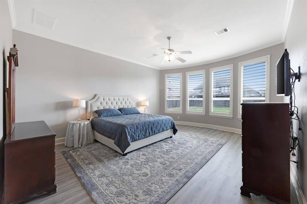The primary suite is a spacious and inviting retreat, featuring elegant crown molding that adds a touch of sophistication to the room. A ceiling fan ensures a comfortable atmosphere, providing a cool breeze on warm days. The bay window creates a cozy nook with natural light pouring in, offering a perfect spot to relax or enjoy the view outside.
