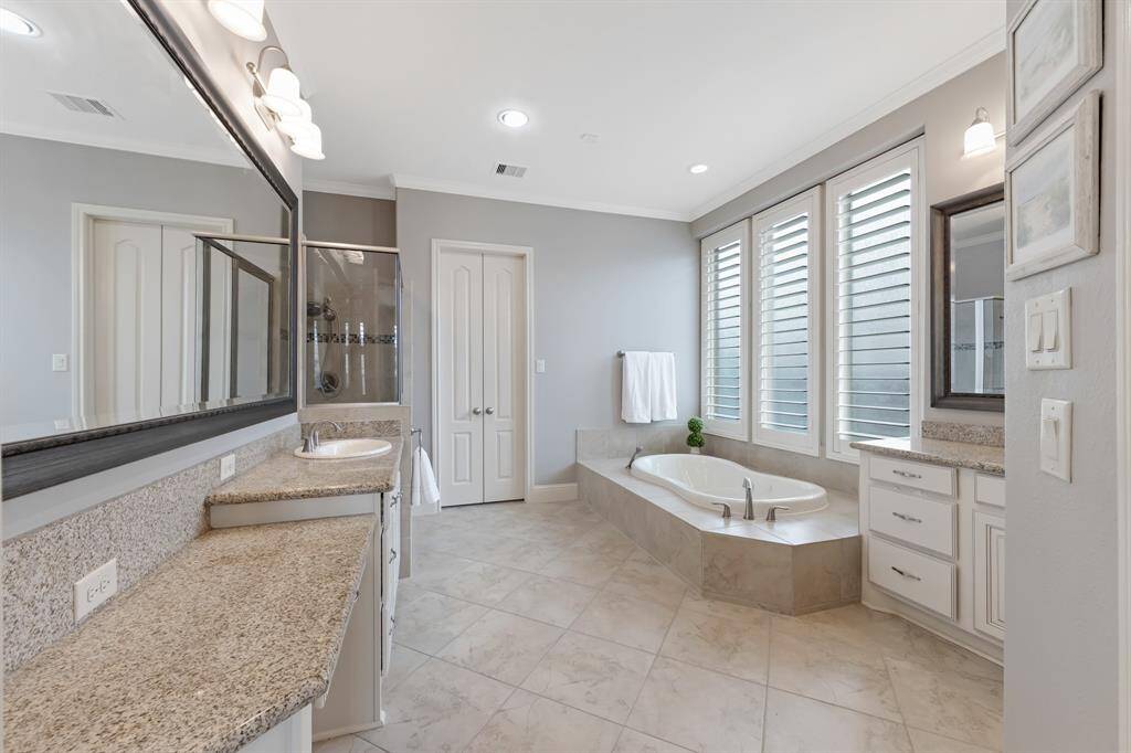 The primary ensuite is designed for both functionality and luxury, featuring his and her vanities with beautiful granite countertops. Framed mirrors add a refined touch, while the crown molding enhances the room's elegant feel. The large walk-in closet offers ample space, complete with built-ins for organized storage and a full-length mirror for convenience and style.