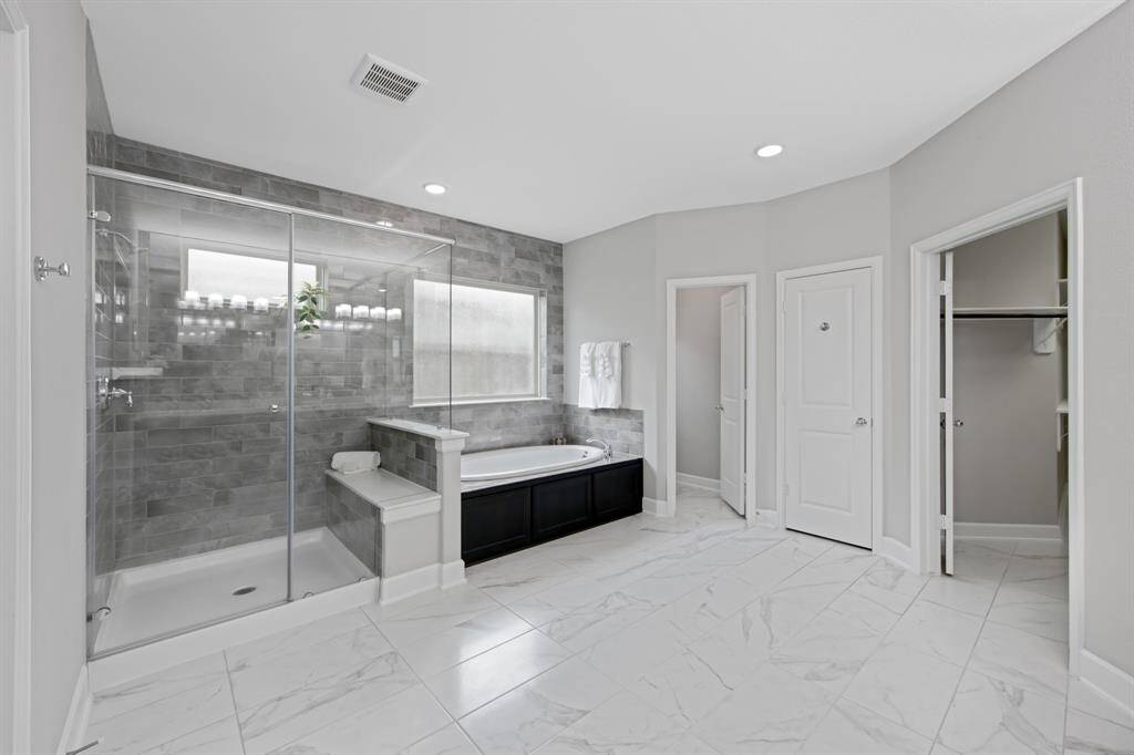 The Primary Bath has an oversized frameless glass shower with a bench and shelf. The entire wall above the tub and in the shower is "floor to ceiling" tile (except the window).
