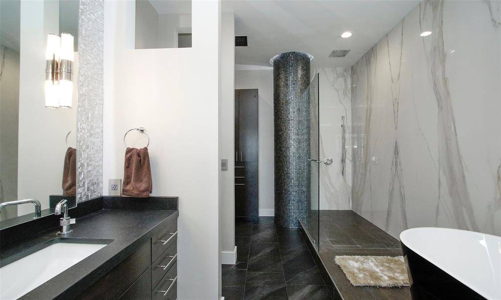 Dekton Silestone walls and frameless glass showcase this large walk-in shower that features a Rain Shower with all the bells and whistles. Decorative mosaic tile and florescent lighting above the column and under cabinets illuminates this modern bathroom that is sure to impress.