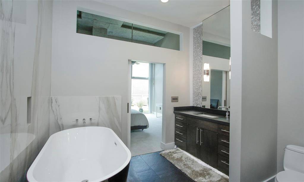 Relax in this porcelain soaking tub while also taking in the downtown view.  Luminous vanity has slate counters, custom cabinetry, a wall of aluminum tile, and Restoration Hardware sconce lighting. Legrand Adone designer switches control the lighting.
