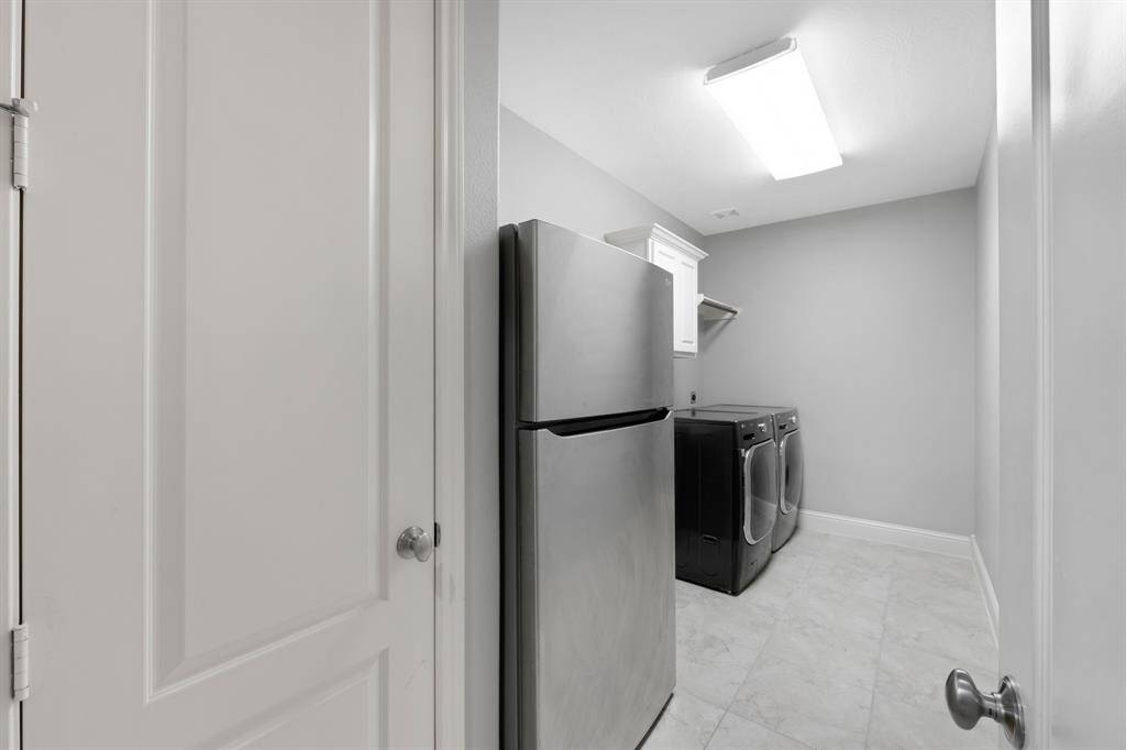 The spacious laundry room is both functional and convenient, featuring a built-in closet for extra storage, a folding table for ease of sorting and organizing, and ample space for a fridge, making it the perfect area for all your laundry needs.