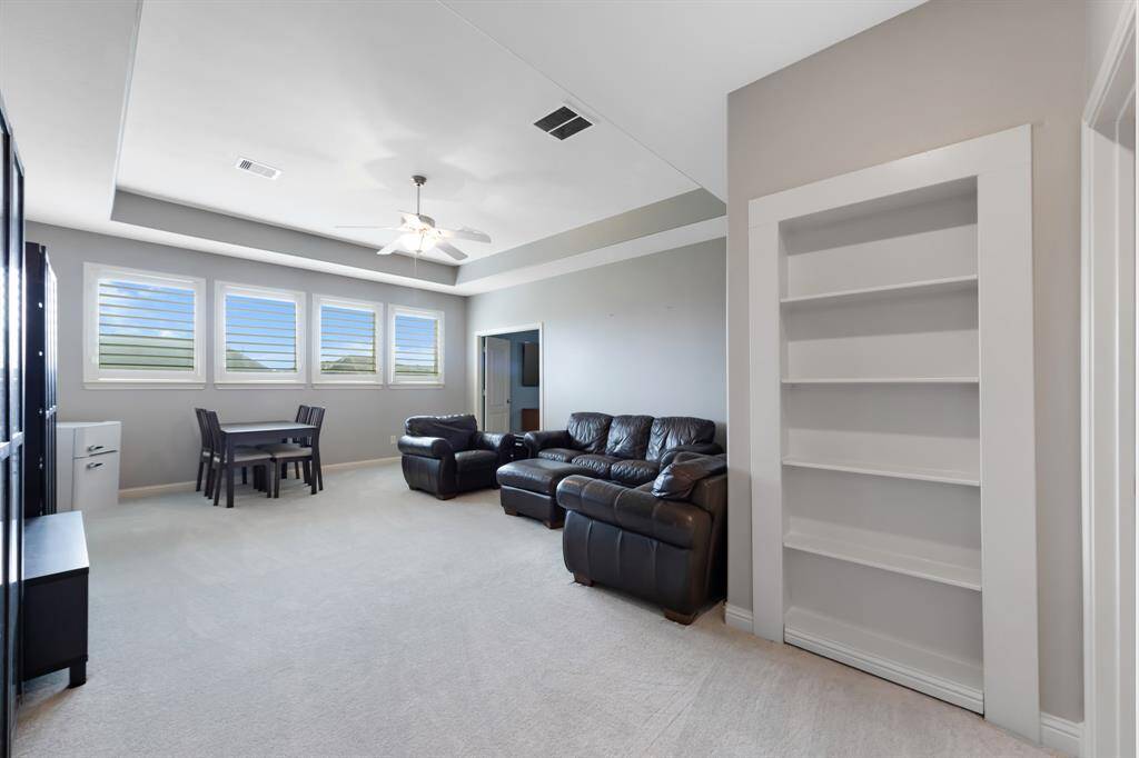 The game room is a vibrant and fun space, featuring a striking tray ceiling that adds depth and elegance to the room. A ceiling fan helps keep the area comfortable, making it an ideal spot for both relaxation and entertainment. One of the most exciting features is the hidden extra room cleverly concealed behind the bookcase.