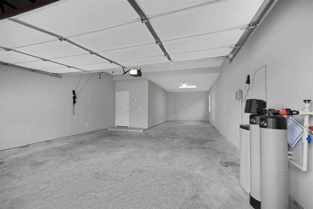 The oversized 3 car tandem garage has a man door to the side yard and a window which provides natural lighting. The water softener is located on the right of this image.  There is an overhead bike hoist mounted to the ceiling as well as an overhead storage rack (in image blocked by garage door).