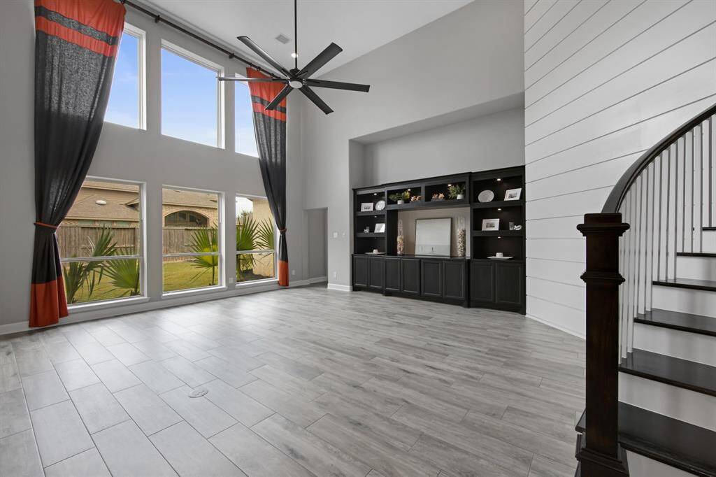 The living room has many upgrade features: wide "shiplap" trim feature on wall ($1,500.00), custom built-in cabinets ($11,640.00)with puck lights ($1,450.00), oversized Kichler Szeplo II LED 80" ceiling fan ($713.00) with slider fan control ($54.00), brass trim electrical outlet in concrete floor ($320.00) and floor to ceiling designer curtains.