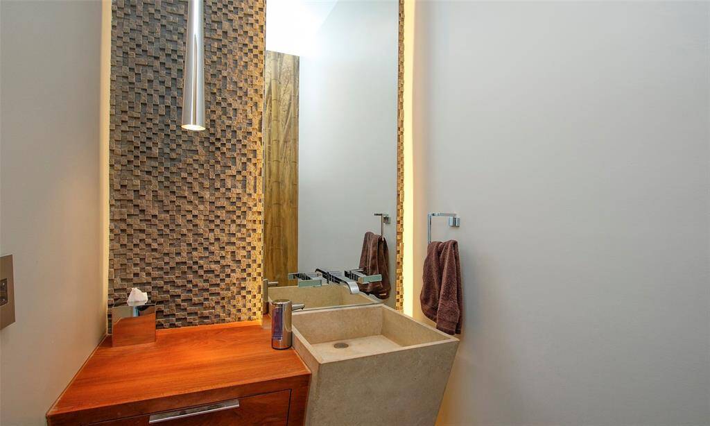 Exquisitely designed powder room. Custom wood cabinetry and Sandstone Pedestal Sink accented with a wall of multi dimensional slate mosaic tile.  Lighting illuminates the Alex Turco designed bamboo forest gold wall art that is floor to ceiling on the back wall.