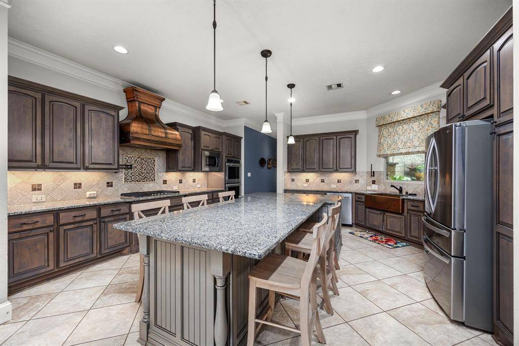 This spacious kitchen features elegant dark wood cabinetry, a large granite island with seating, stainless steel appliances, and a stylish tiled backsplash. Perfect for entertaining and family gatherings.