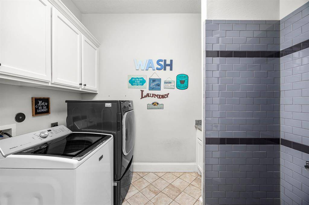 This photo shows a well-organized laundry room with a washer and dryer set, white cabinets for storage, decorative wall signs, and utility shower.