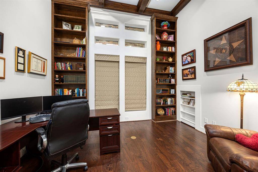 Cozy home office with rich wood flooring and built-in bookshelves flanking large windows.