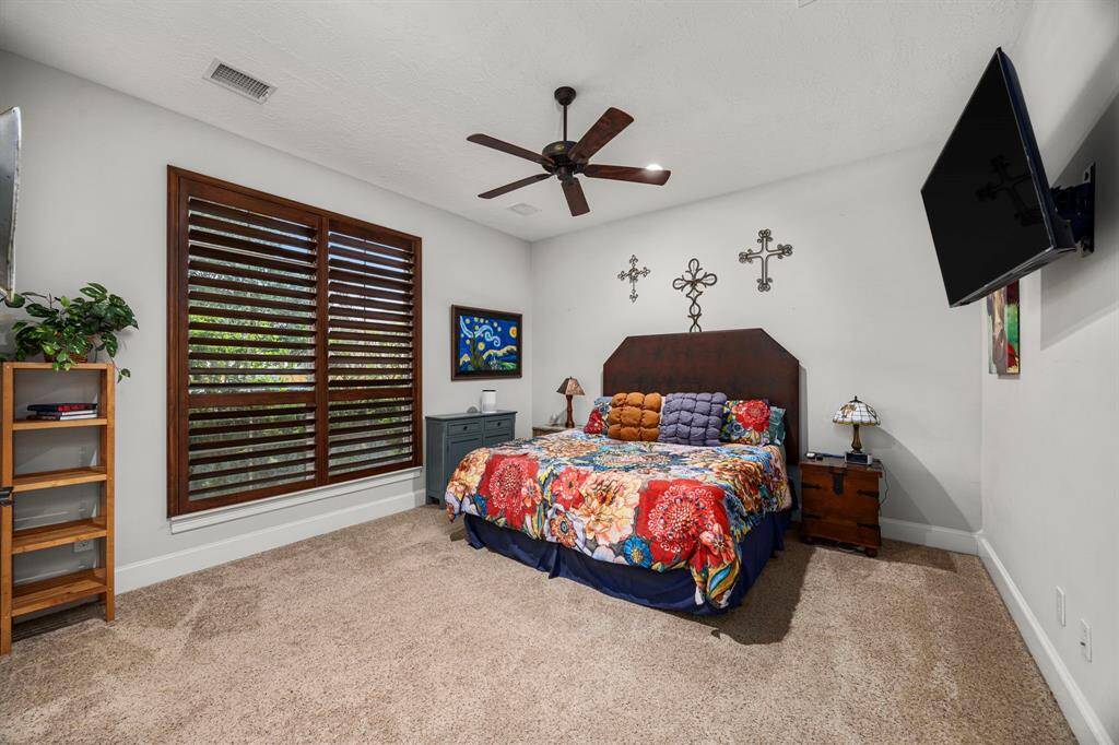 Secondary Bedroom located on first floor features a large window with wooden shutters, a ceiling fan, and carpeted flooring