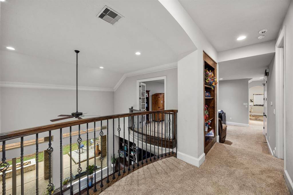 Upstairs hallway with carpeted flooring, featuring an elegant iron railing overlooking a lower level. There's a built-in bookshelf and recessed lighting, adding a modern touch.