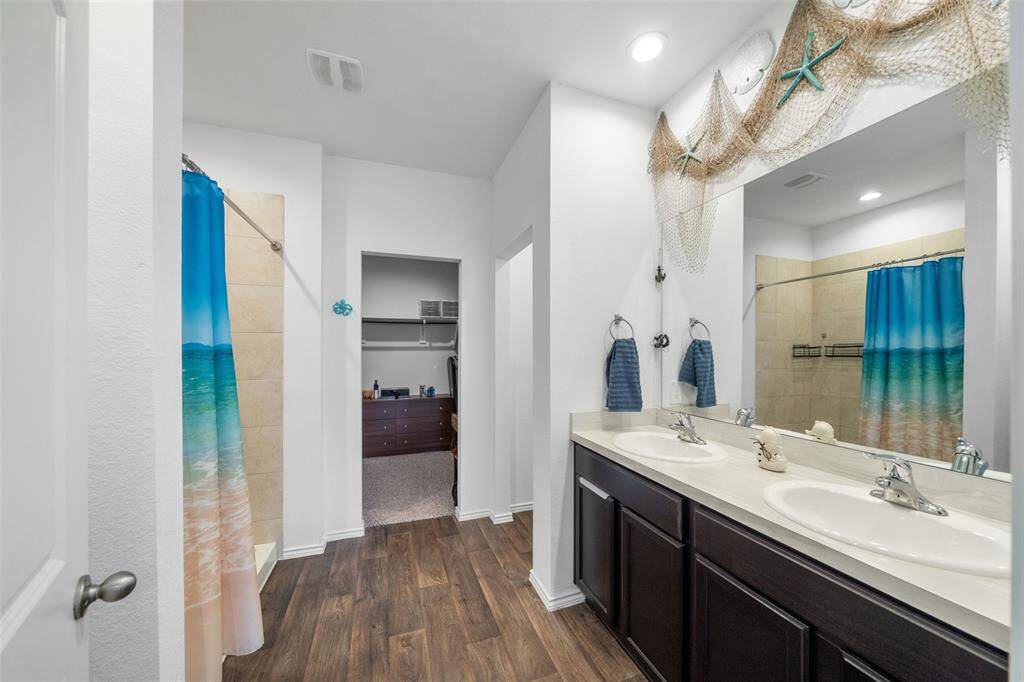 A view of the primary en suite with double sinks and large walk in shower. Ample sized closet and water closet beyond the sinks.