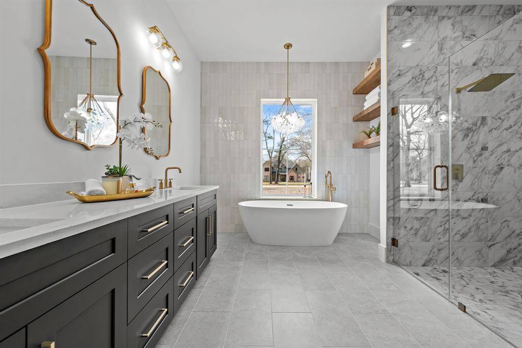 Stunning primary bath with double vanities, oval vessel tub, floating shelves, floor to ceiling tile, large walk in shower and private water closet.