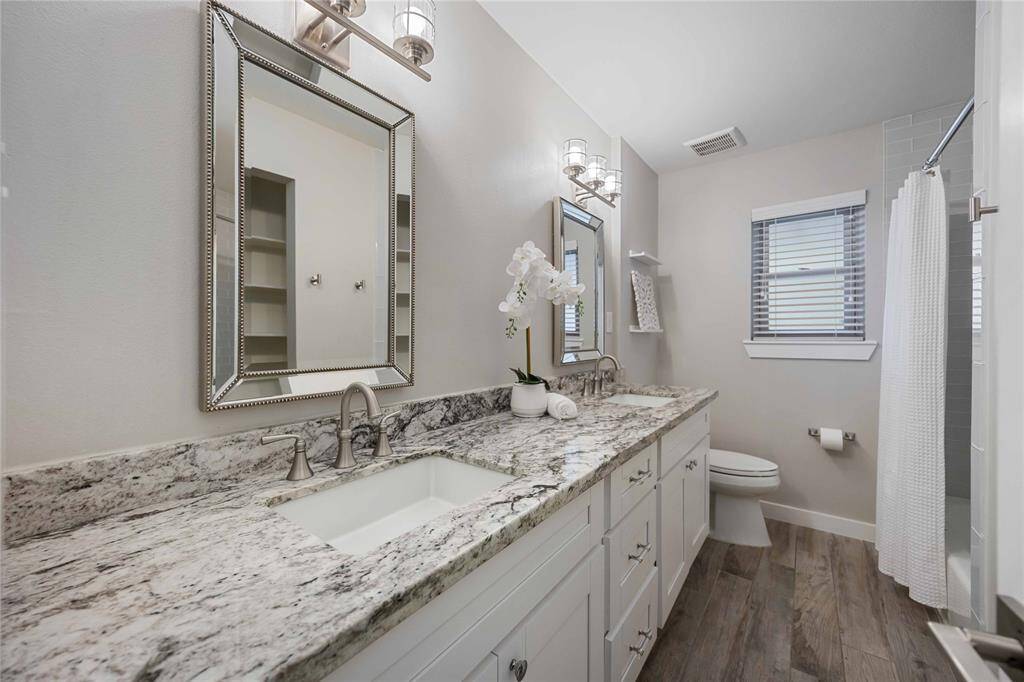 A large hallway bath features a lengthy granite-topped vanity that rests under beautifully framed mirrors.