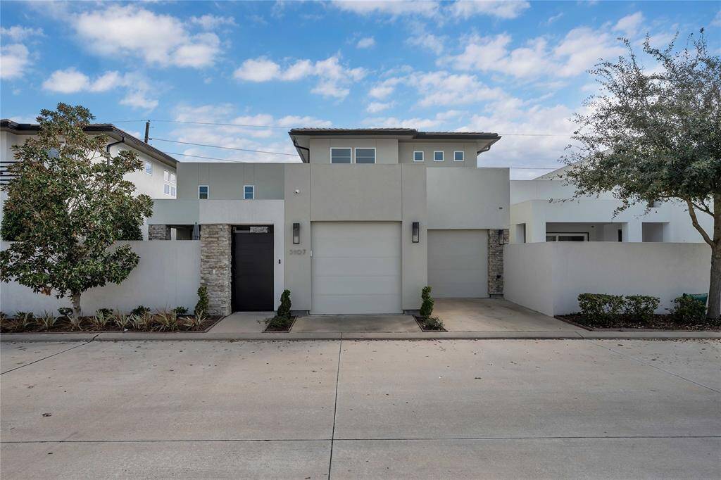 This modern home features a sleek facade with a minimalist design. It includes a private entryway with stone accents, and is framed by landscaped greenery. The flat roof and clean lines enhance its contemporary appeal.